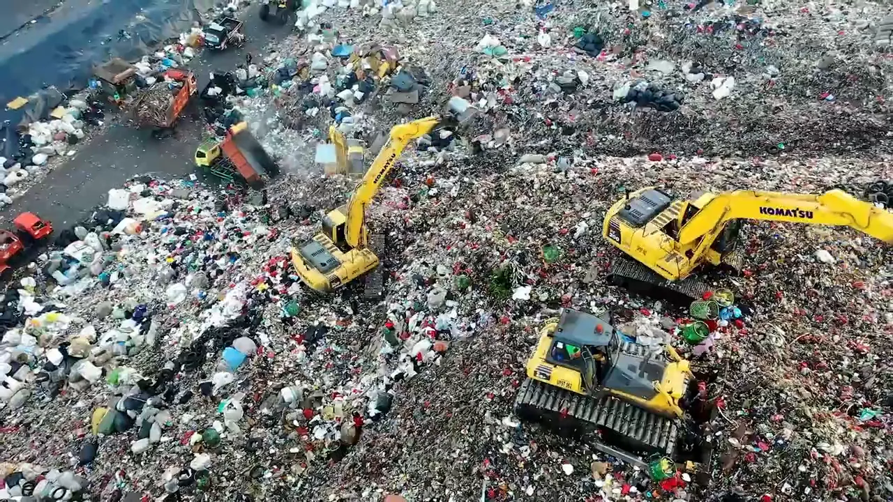 Aerial view of multiple yellow construction machines working in a large waste dumping area