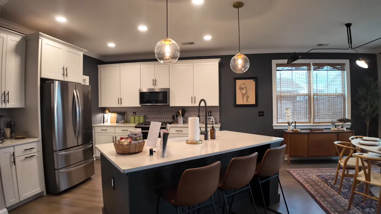 open kitchen with large angled island white cabinets pendant lights stainless refrigerator and dining area