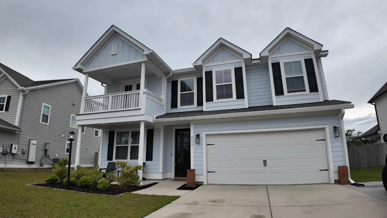 front exterior of a two story light blue house with black shutters balcony and two car garage