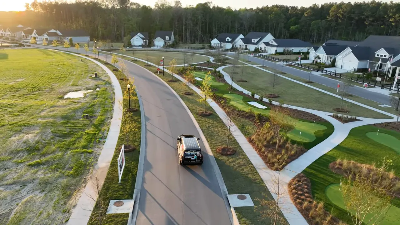 Aerial photograph of a neighborhood street with sidewalks, green spaces, putting greens and homes at sunset