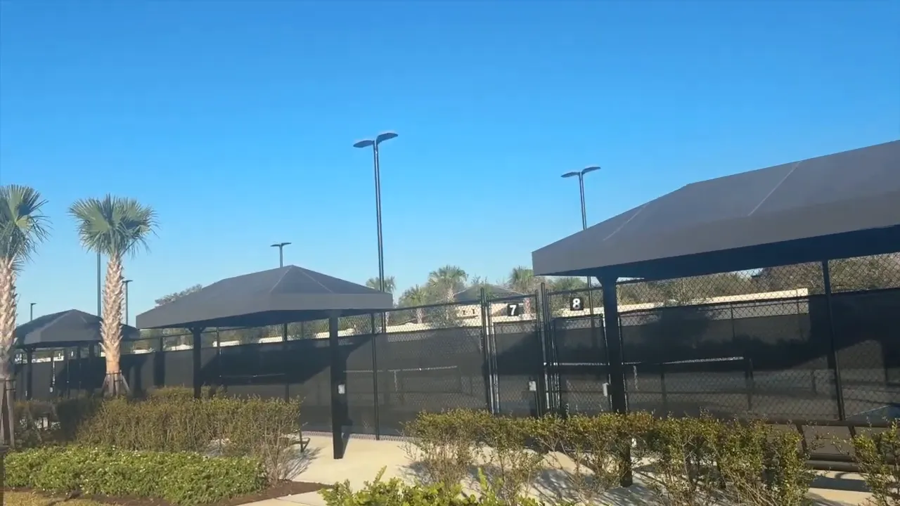 Multiple fenced sports courts with shade structures and palm trees