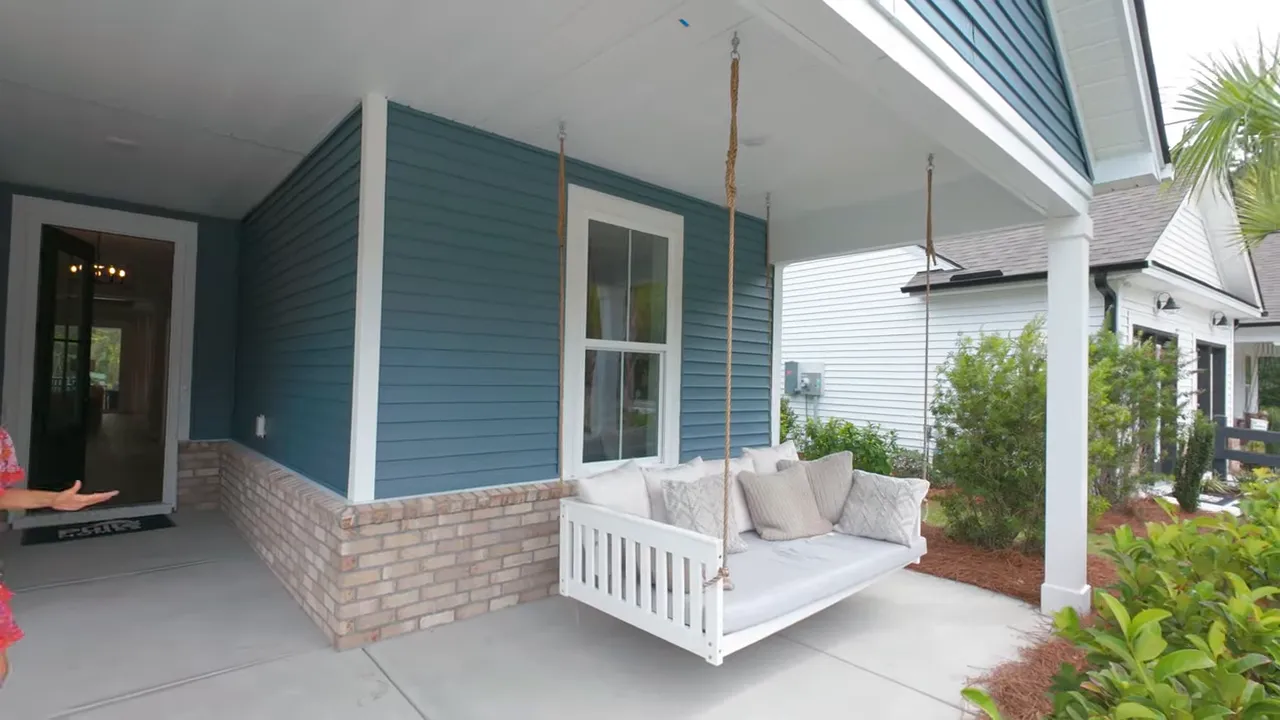 Deep covered front porch with white swing and blue siding