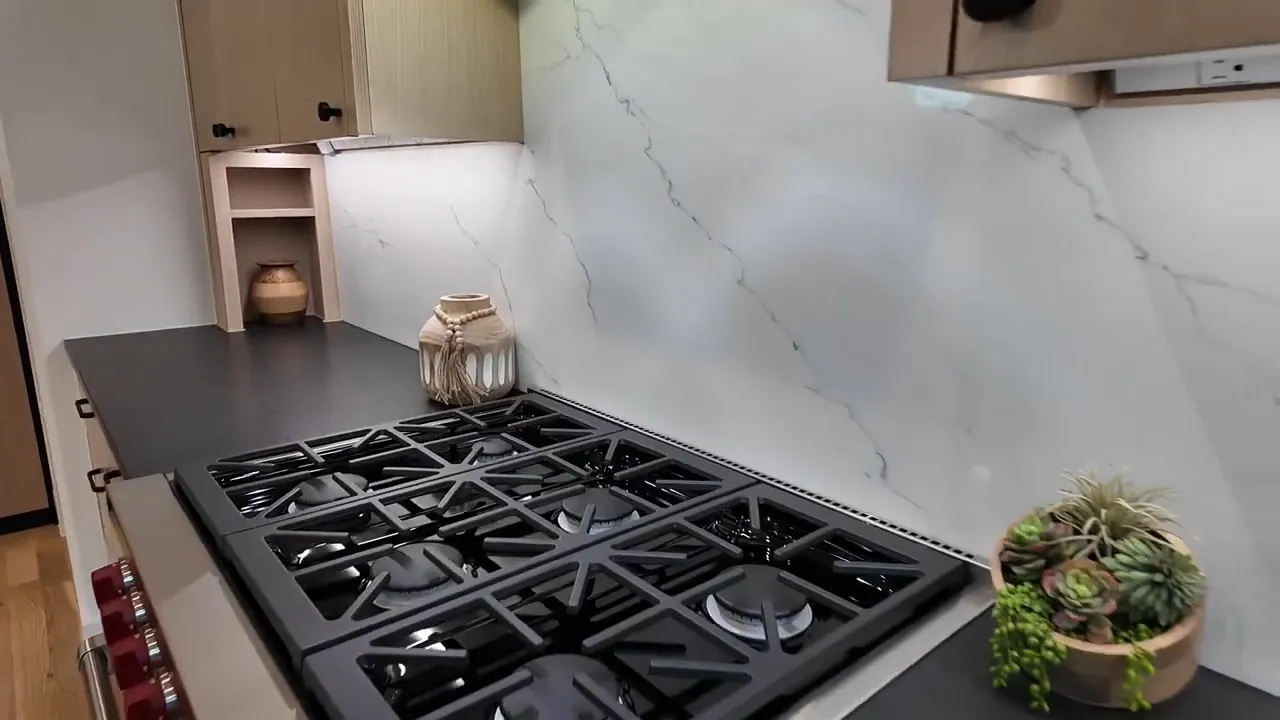 Modern kitchen six-burner gas cooktop with white marble-style backsplash and quartz counters