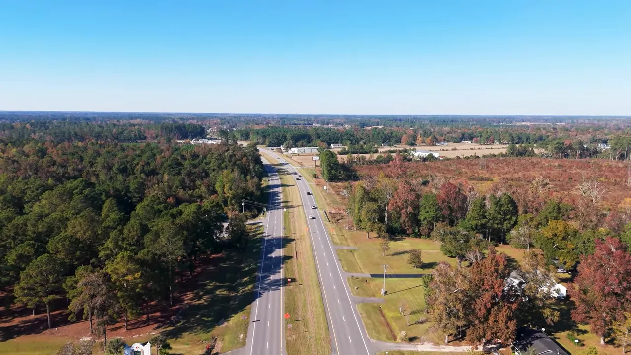 High-resolution drone image of a two-lane divided road through Longs, SC with surrounding trees and fields