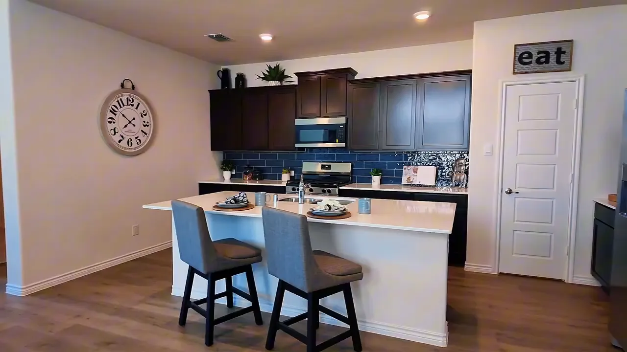 Wide view of kitchen with large island, bar stools, and stainless appliances