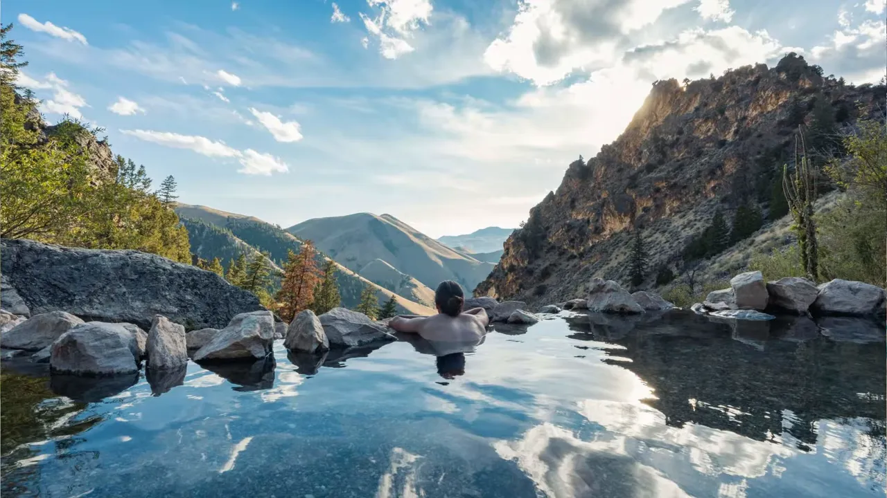 Person relaxing in a mountain hot spring surrounded by rocky cliffs