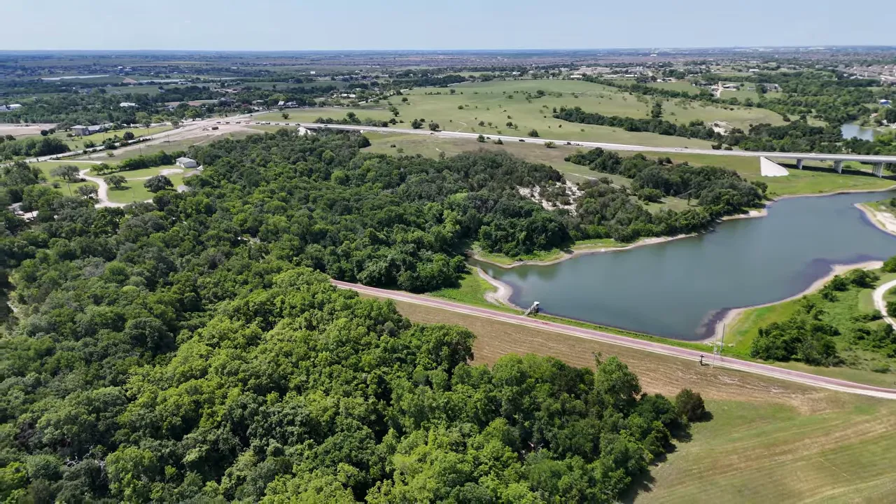 Aerial view of a lake, wooded area and nearby road outside Hutto showing open green space and water