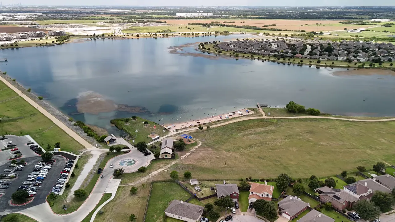 Aerial view of a large lake with sandy beach, docks, walking paths and nearby homes at Lakeside Meadows