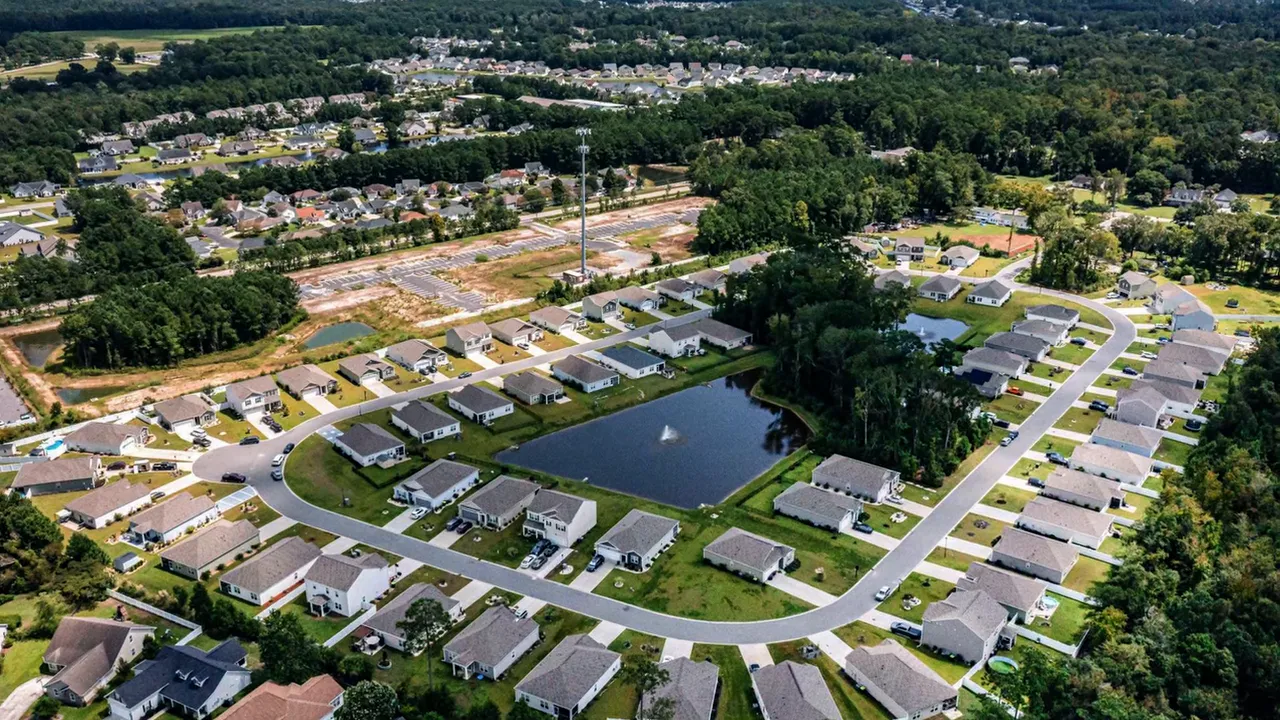 Aerial view of a suburban neighborhood with single-story homes arranged around a pond and green yards.