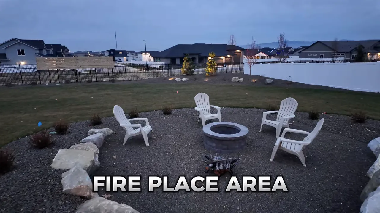 Circular fire pit area with white chairs on gravel in large backyard