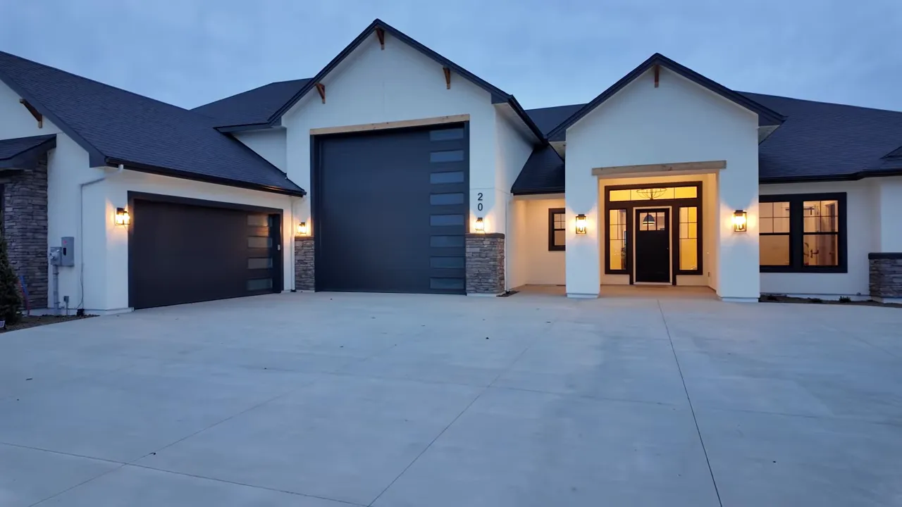 Modern white home exterior with black garage doors and lit entry
