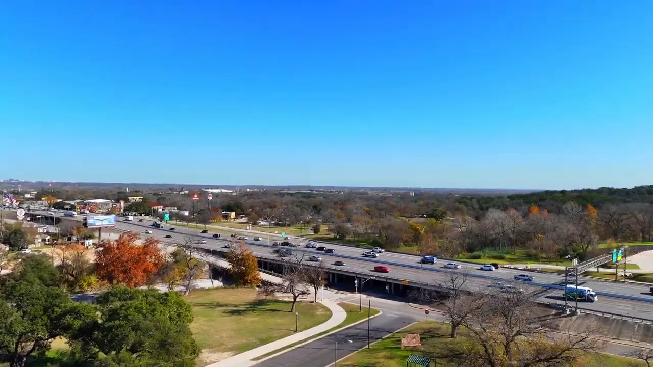 Aerial view of I‑35 in Belton with multi‑lane traffic, an overpass, parkland and trees under a clear blue sky.