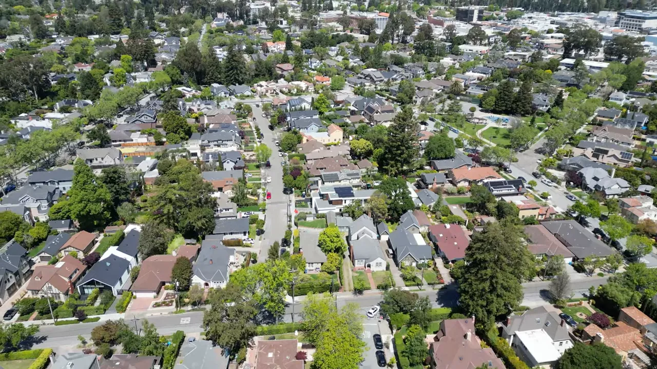 Aerial view of a tree-lined Burlingame-style neighborhood with homes, streets, and nearby green space.