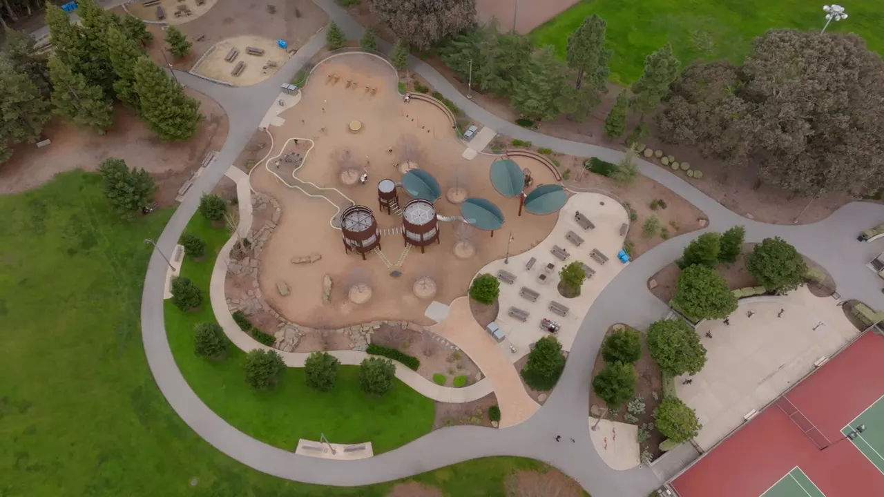 Aerial drone shot of a playground, park paths, and adjacent open green space