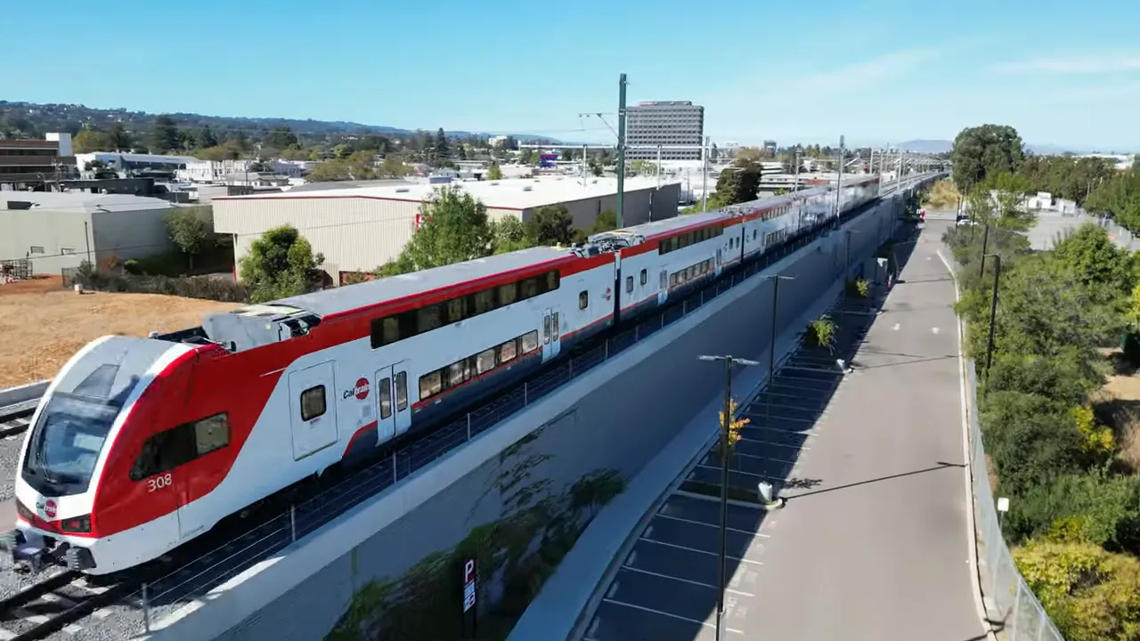 Long view of a modern Caltrain double-decker train traveling on an elevated track next to a parking area