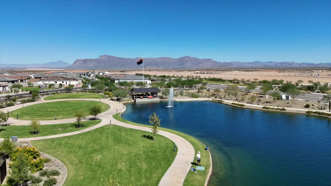 Aerial view of lake with curved walking paths green lawn and mountains