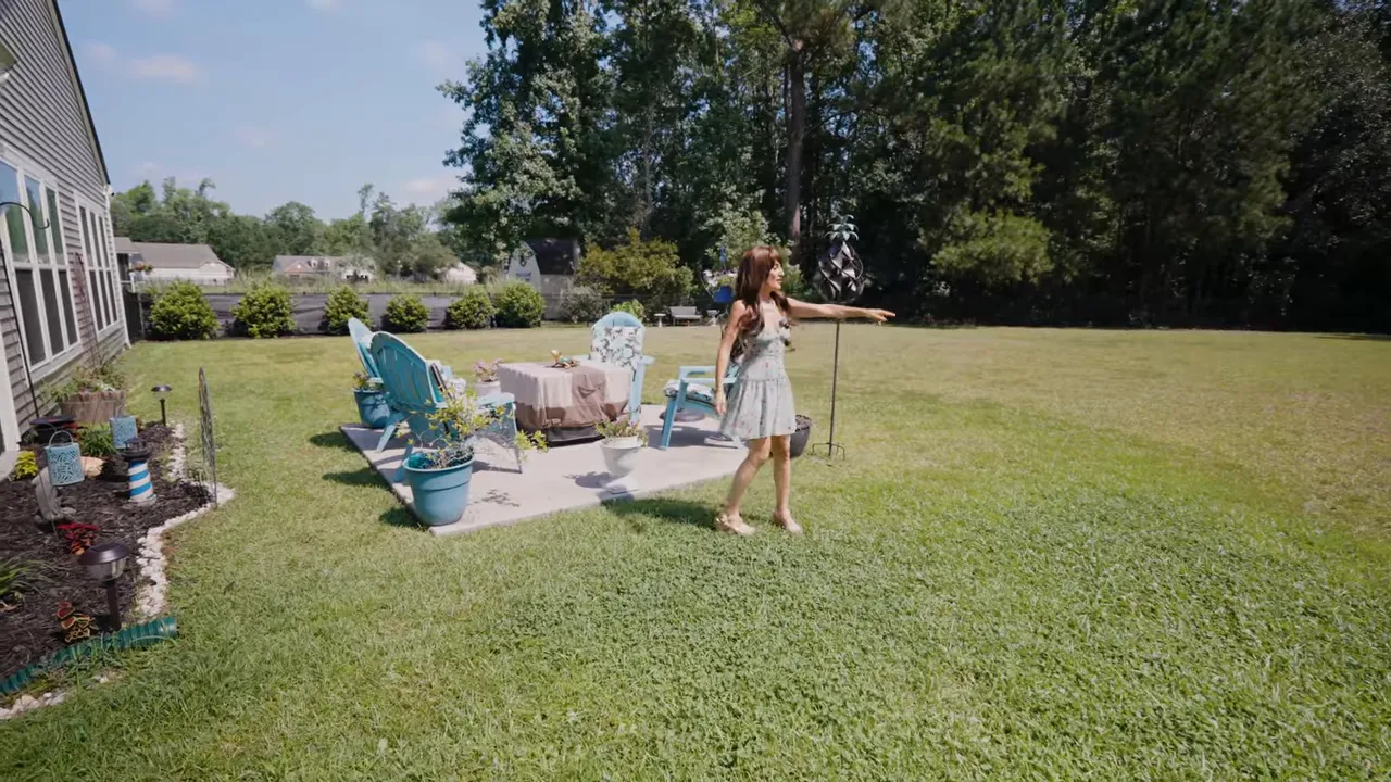 Wide backyard lawn behind house with patio seating and tree line in the distance
