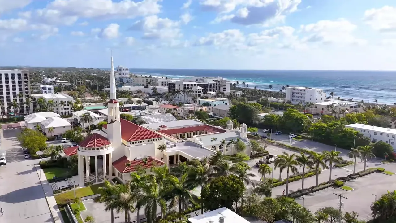 Aerial view of a coastal neighborhood with low-rise buildings, a church tower and the Atlantic shoreline in the background.