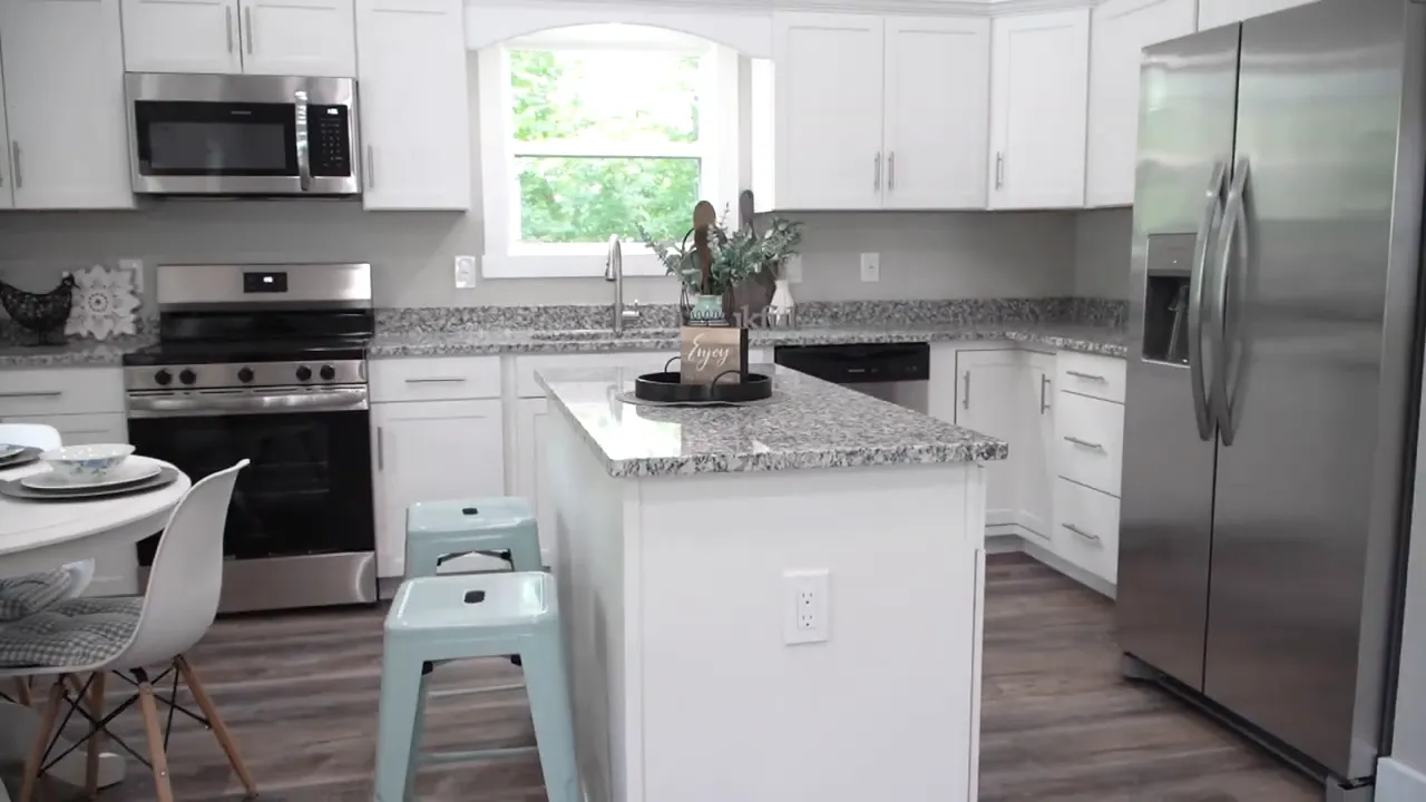 Kitchen with speckled island countertop, white cabinets, stainless appliances, and window over sink