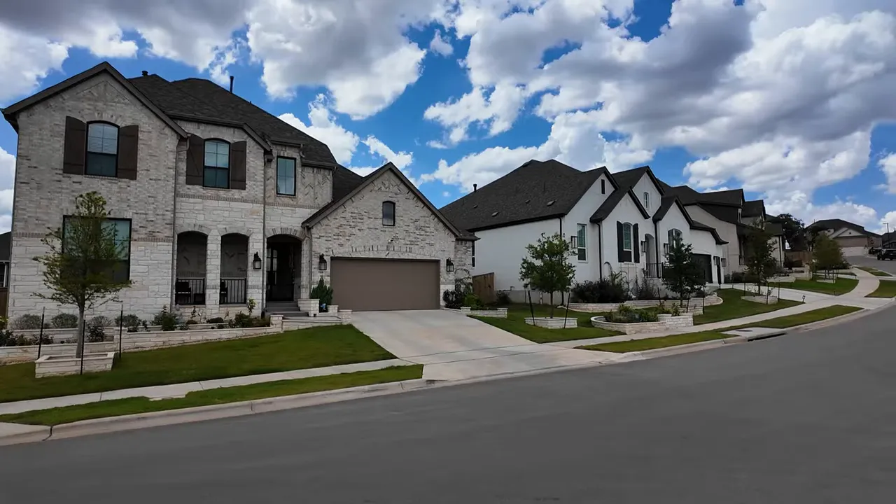 Parkside on the River residential street with stone and stucco homes, driveways and landscaped yards under a blue sky.
