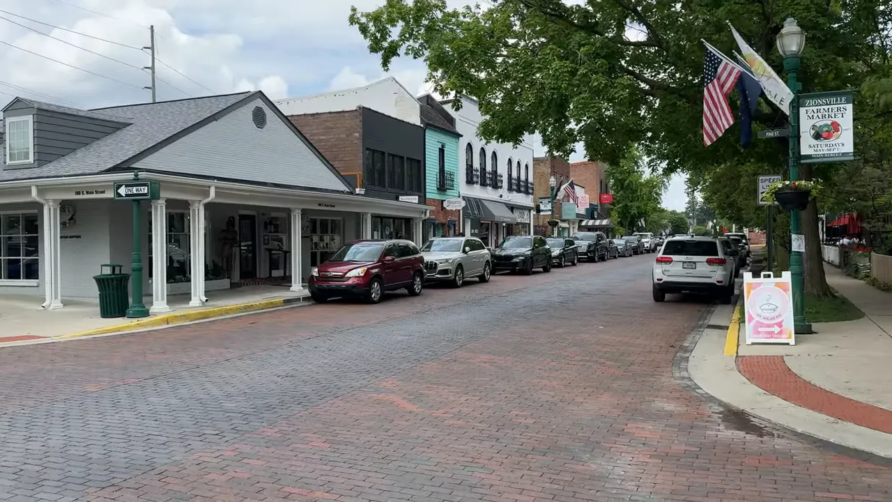 Brick Main Street lined with shops parked cars flags and mature trees