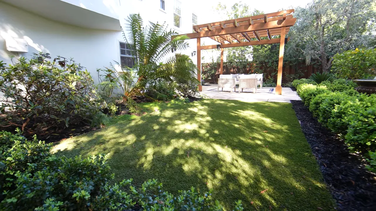 Backyard with green lawn, pergola seating area and surrounding shrubs