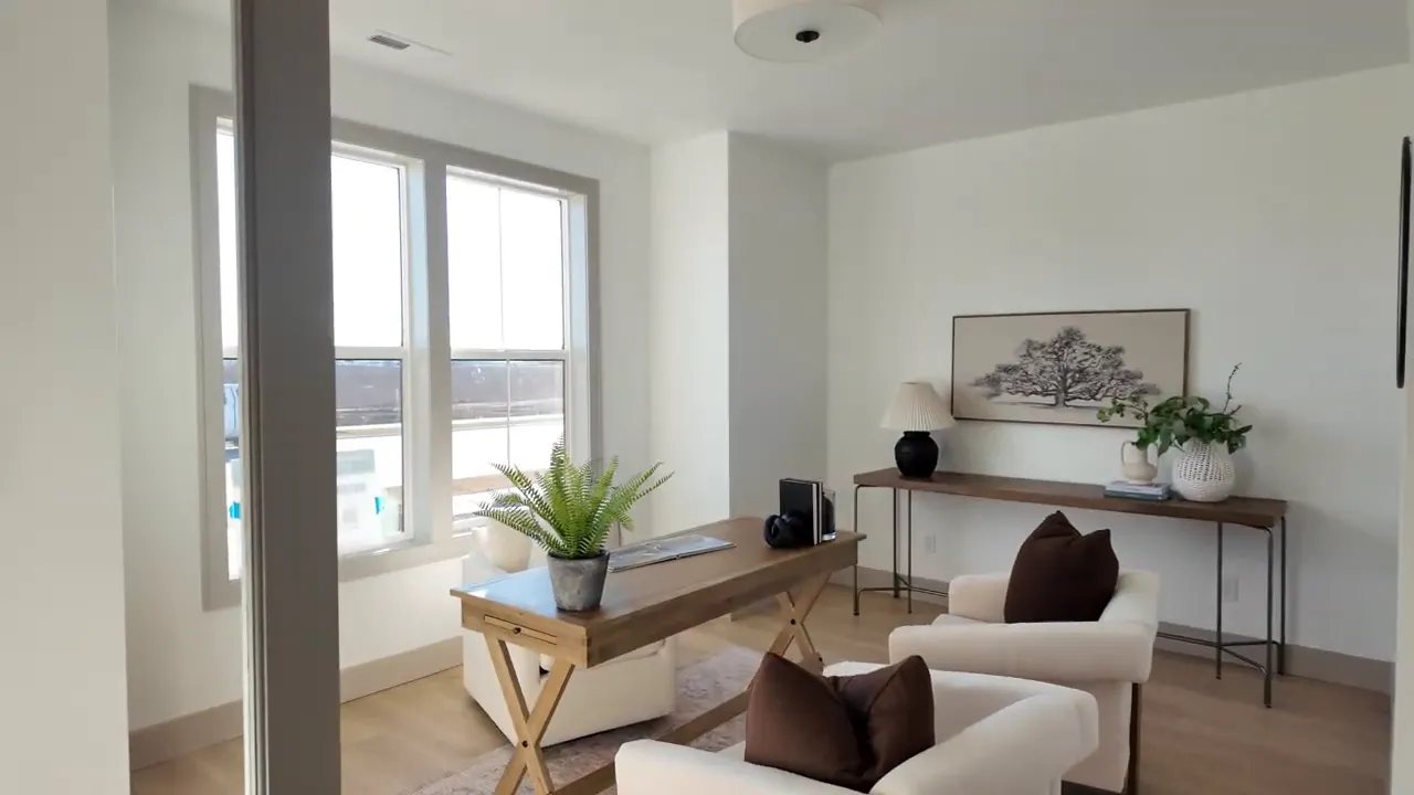 Bright home office with a wooden desk, two armchairs, potted plant, and large windows