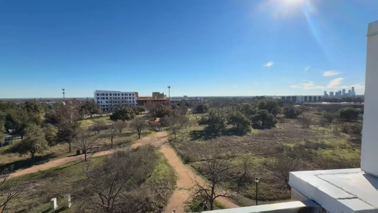 Rooftop deck view over adjacent park with walking paths and the Austin skyline on the horizon under a clear blue sky.
