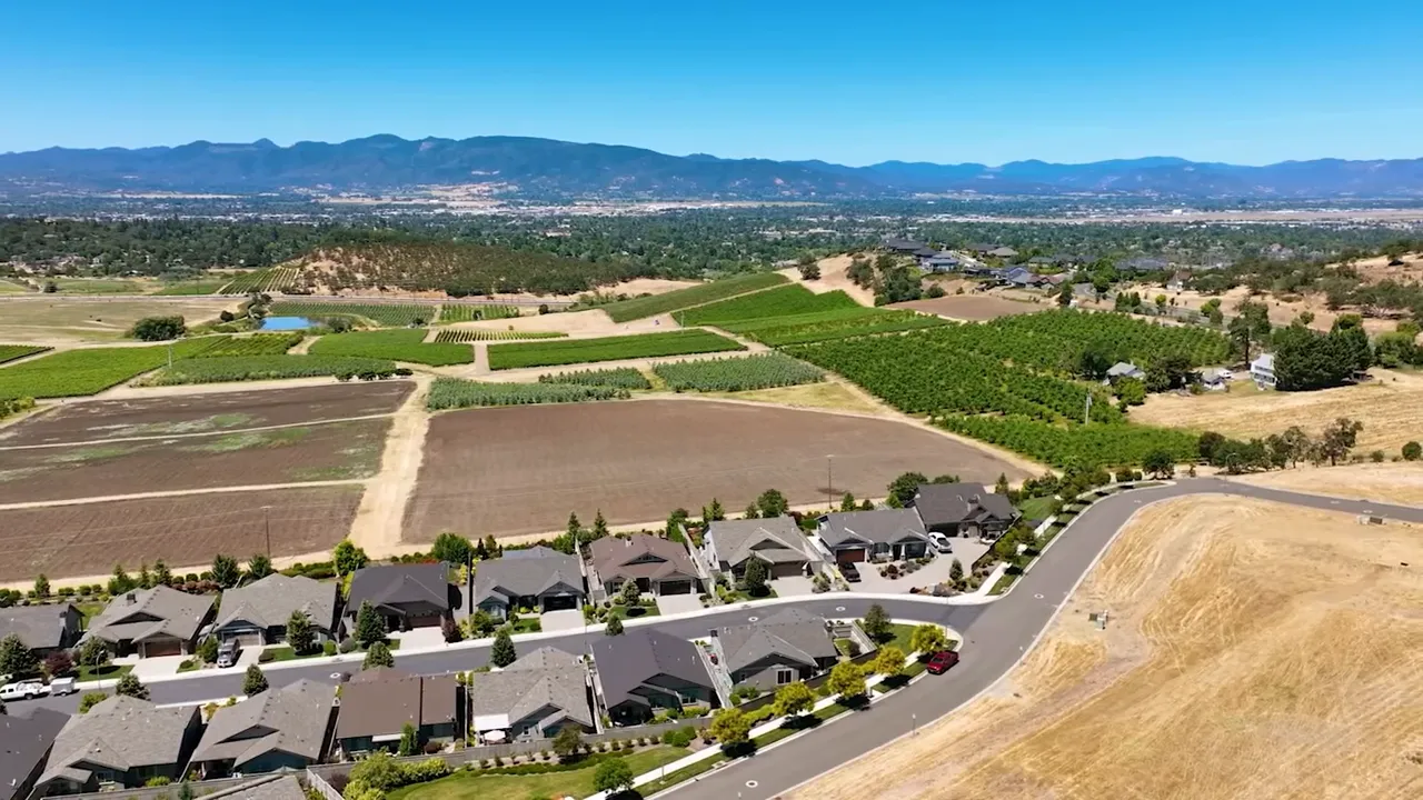 wide aerial landscape showing rows of homes adjacent to open fields and hills with mountains in the distance