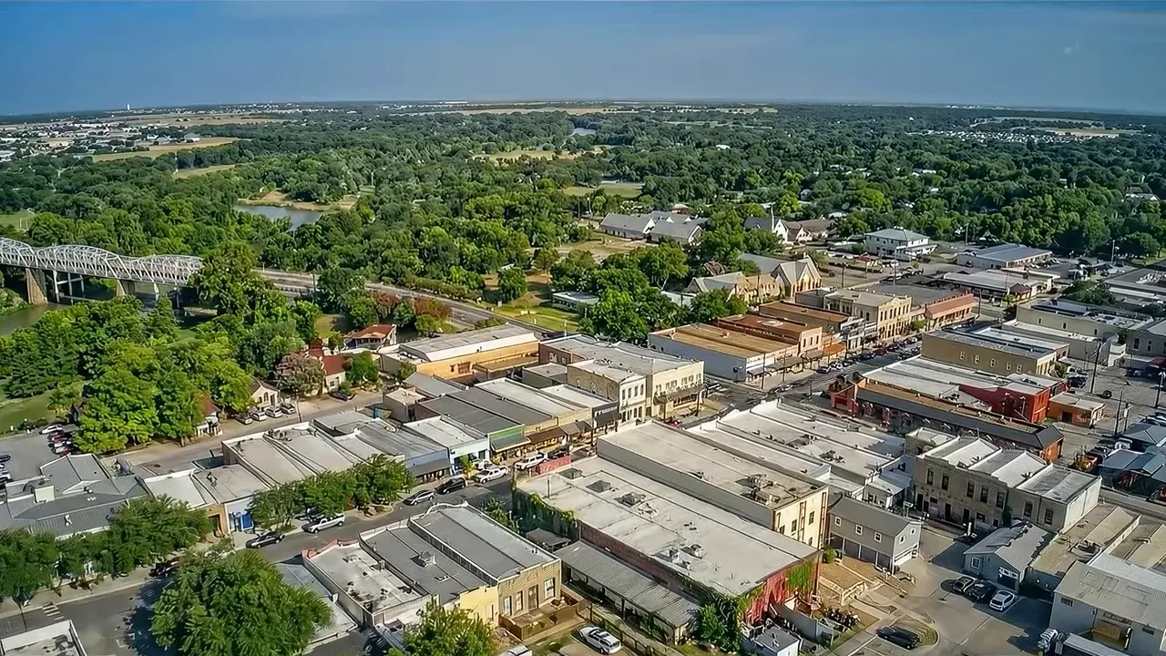 Aerial view of a small town downtown with a bridge, river, and surrounding pine trees