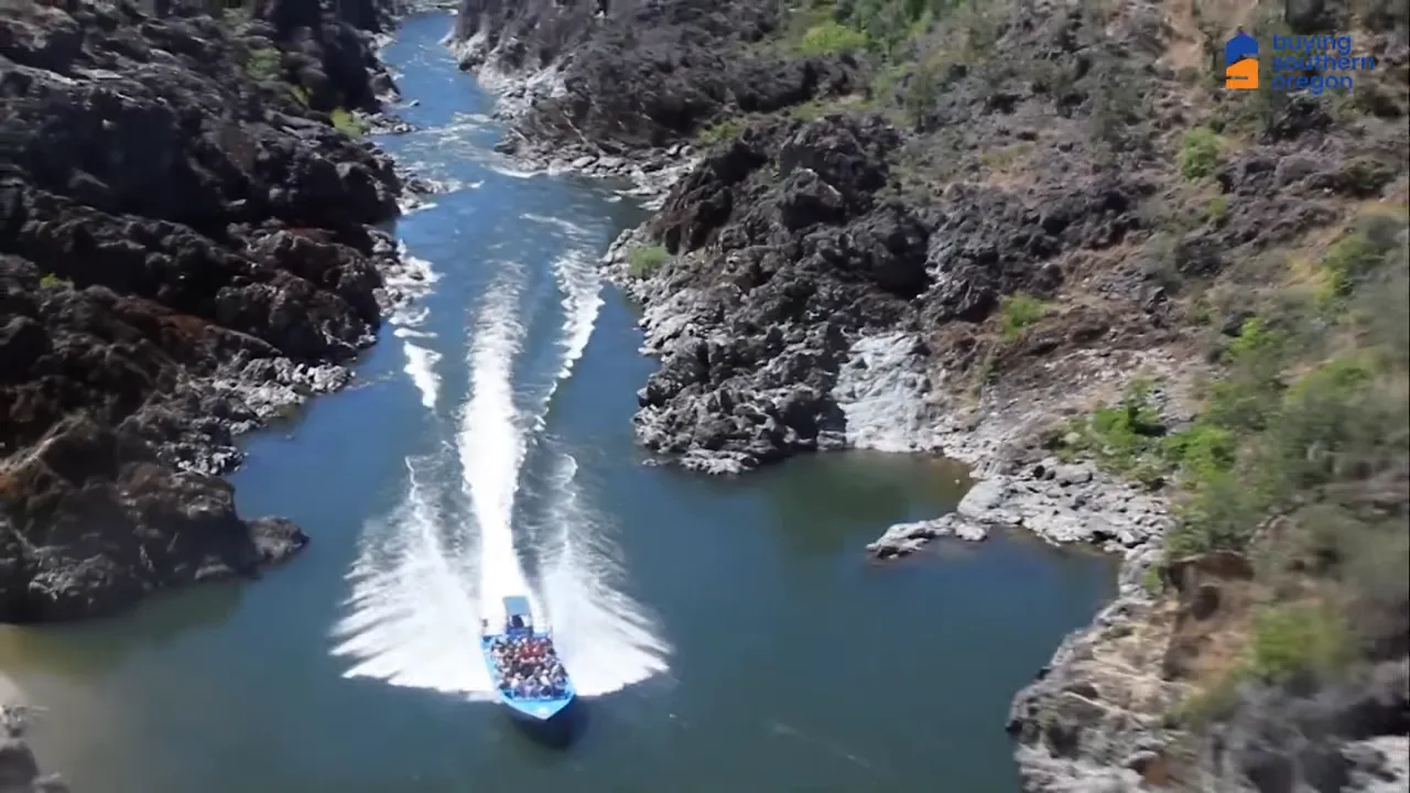 Blue jetboat speeding through a narrow rocky canyon on the Rogue River leaving a large wake behind.