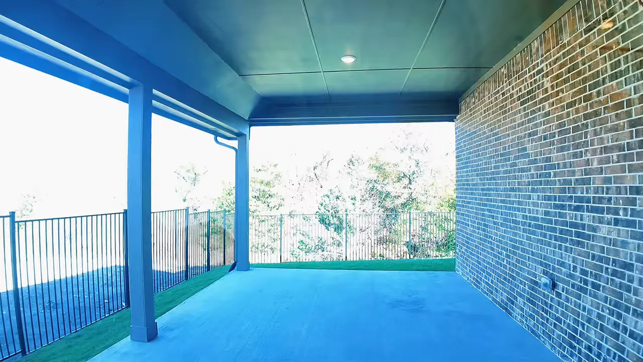 Large covered back patio with brick wall and black metal fence beyond