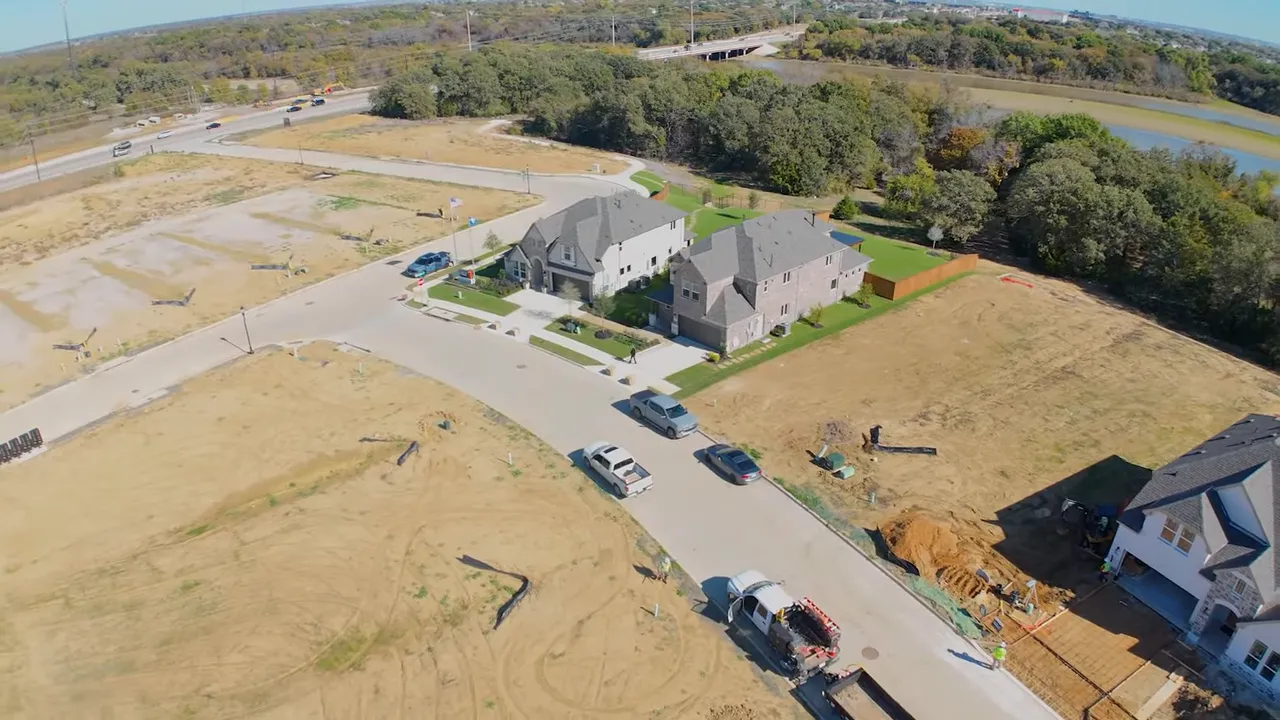 Aerial drone view of new construction homes, empty lots, street and lake treeline at Spiritus Ranch Little Elm, Texas.