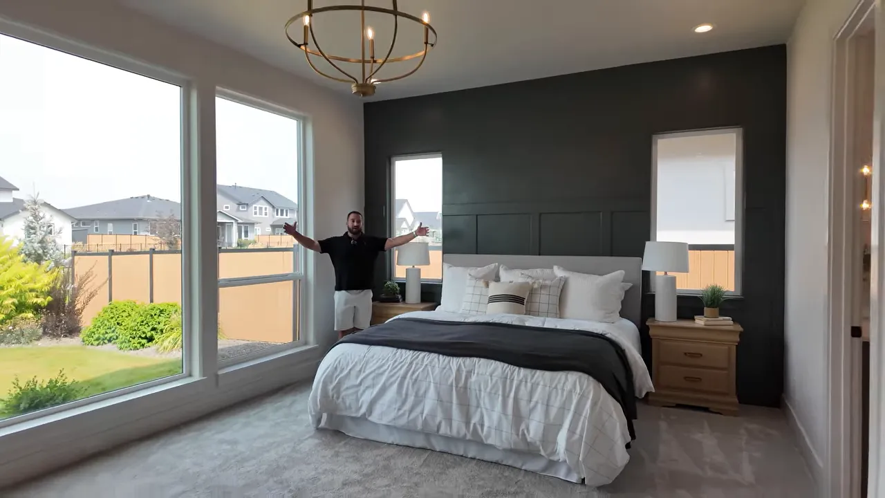 Spacious primary bedroom with large windows bed and dark accent wall