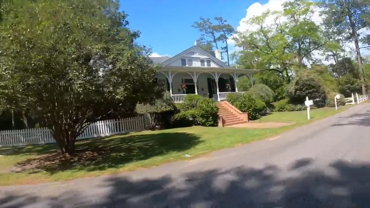Historic style home with wide porch and large yard along tree lined road