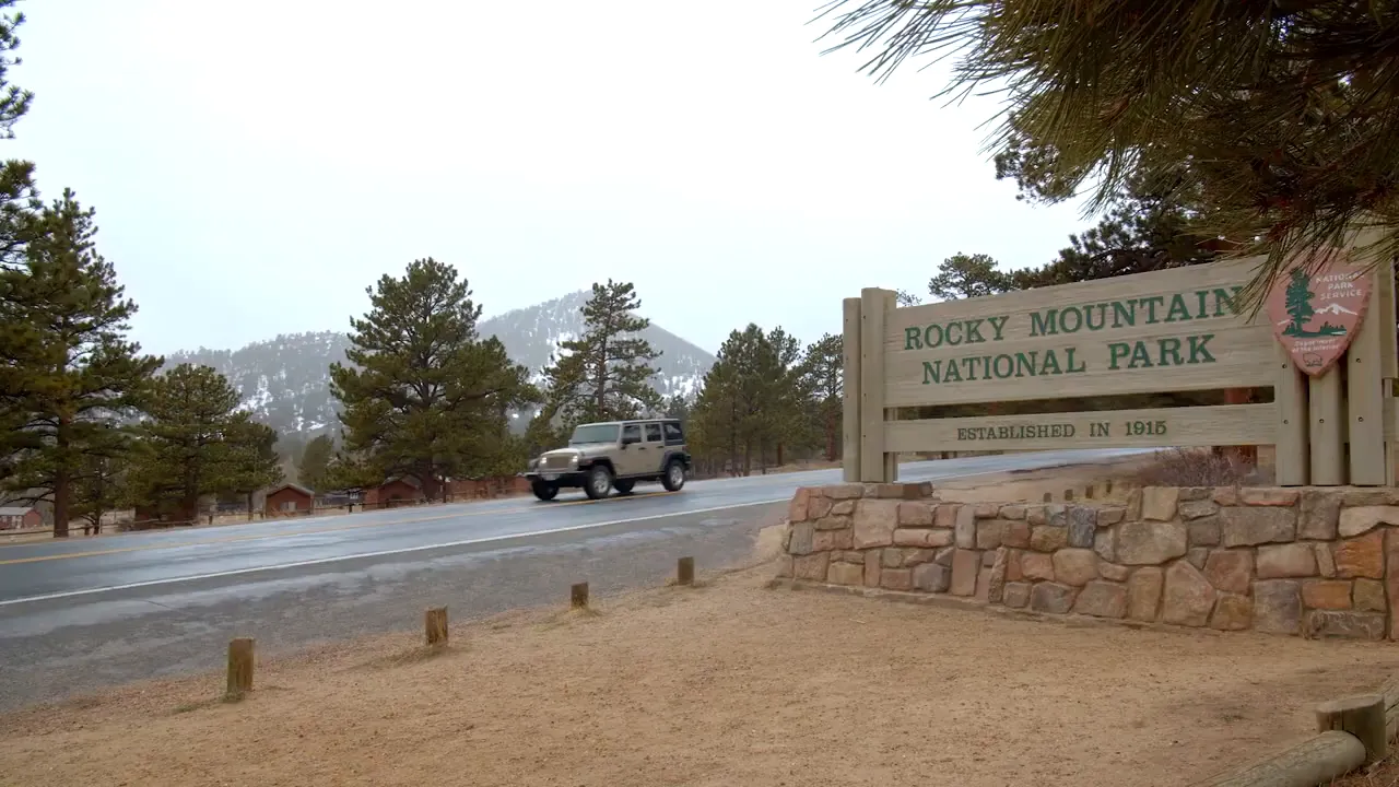 Rocky Mountain National Park entrance sign beside a road and pine trees