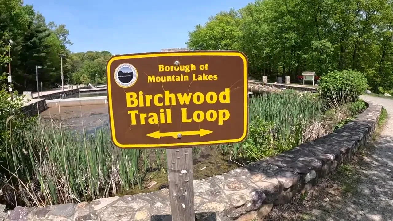 sign reading borough of mountain lakes birchwood trail loop beside a lakeside path