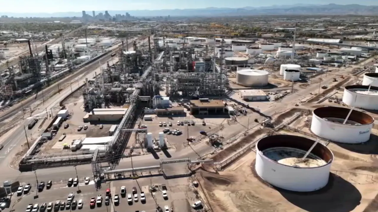 Industrial tanks, facilities, and rail corridor with city skyline in distance