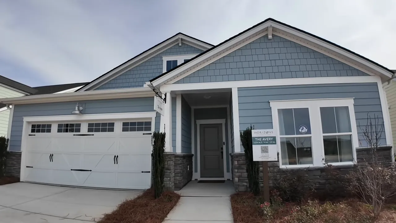 Front exterior of The Avery model home with light-blue hardy plank siding, stone knee wall, two-car garage, and a yard sign reading 'The Avery'.