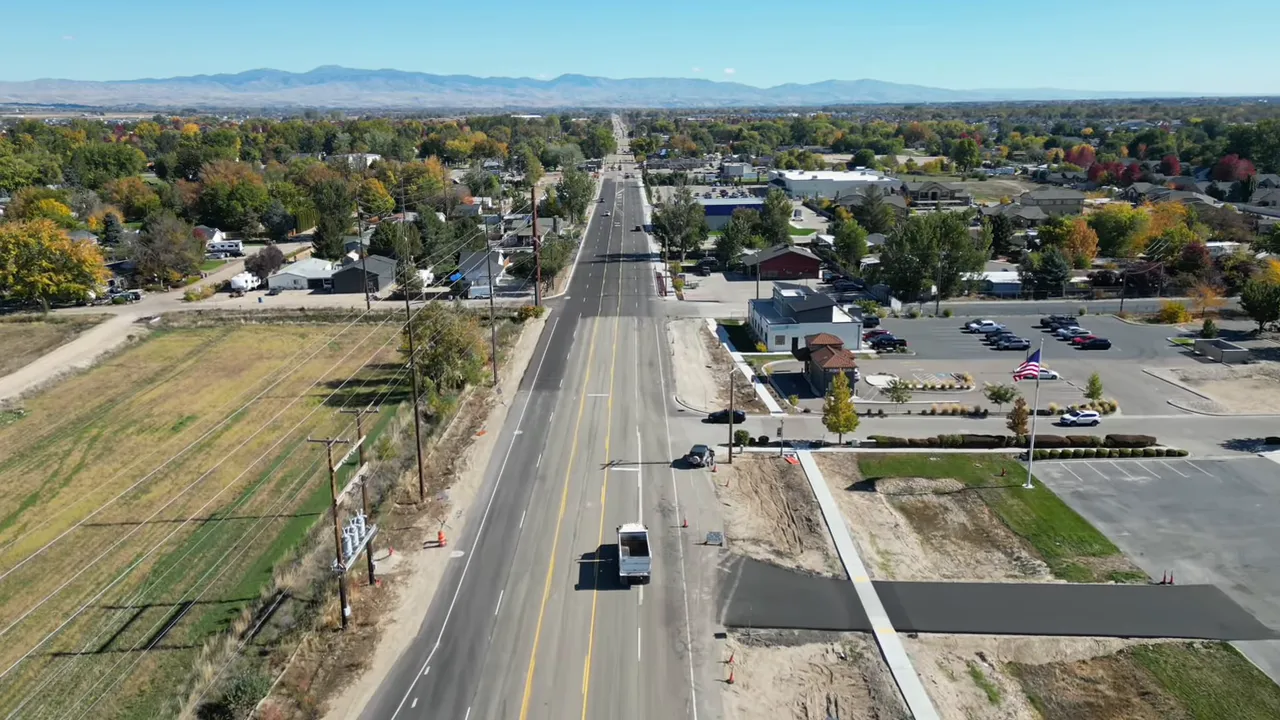 Straight aerial shot down a suburban road with residential areas on both sides and mountains on the horizon.