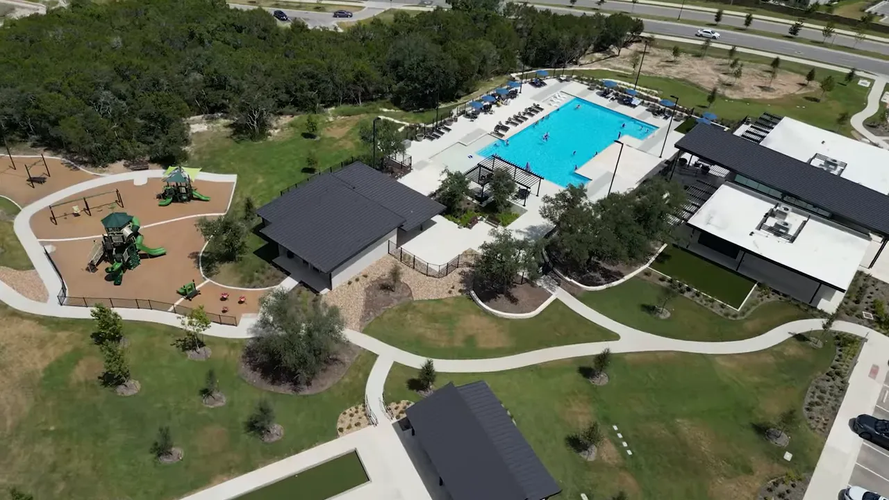 Aerial view of a large turquoise community pool with lounge areas and buildings