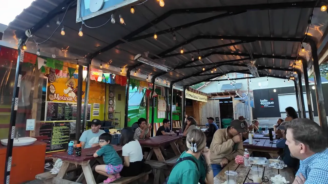 Covered outdoor food cart seating area with people eating at picnic tables