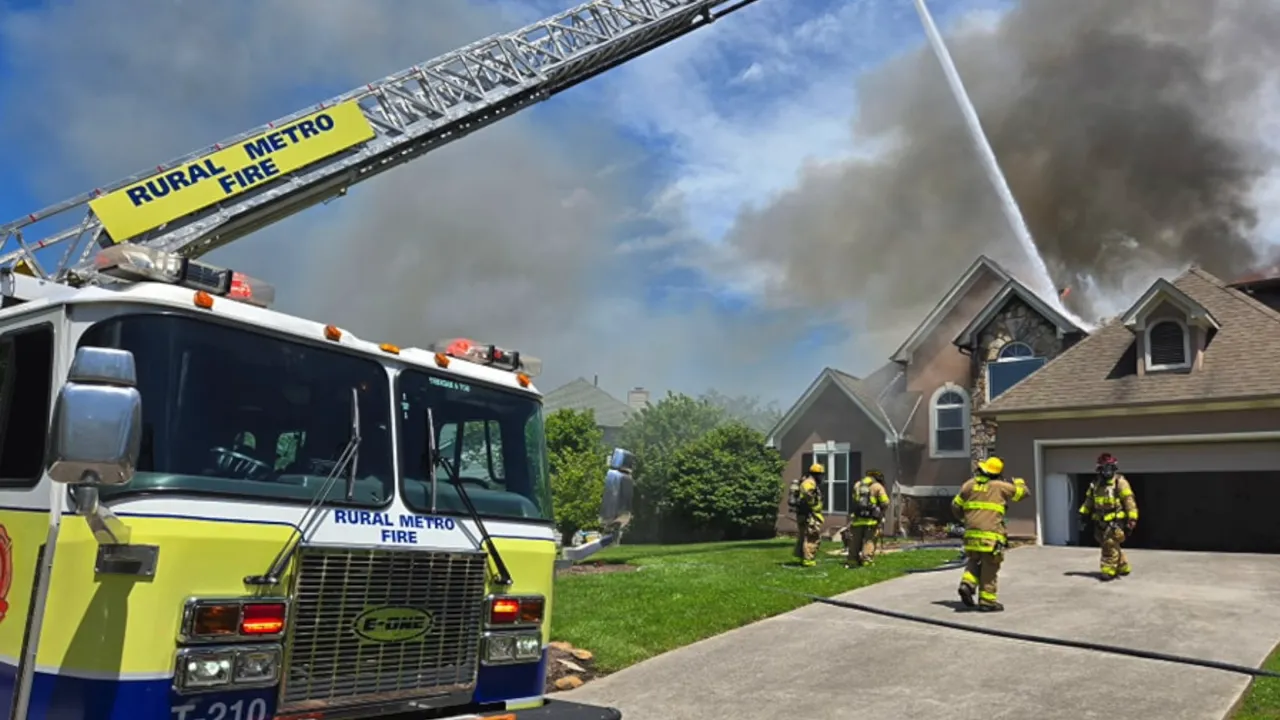 Fire truck and firefighters spraying water on a house fire with smoke rising