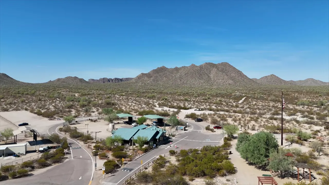 Desert parking area and trailhead buildings with San Tan Mountains in the distance