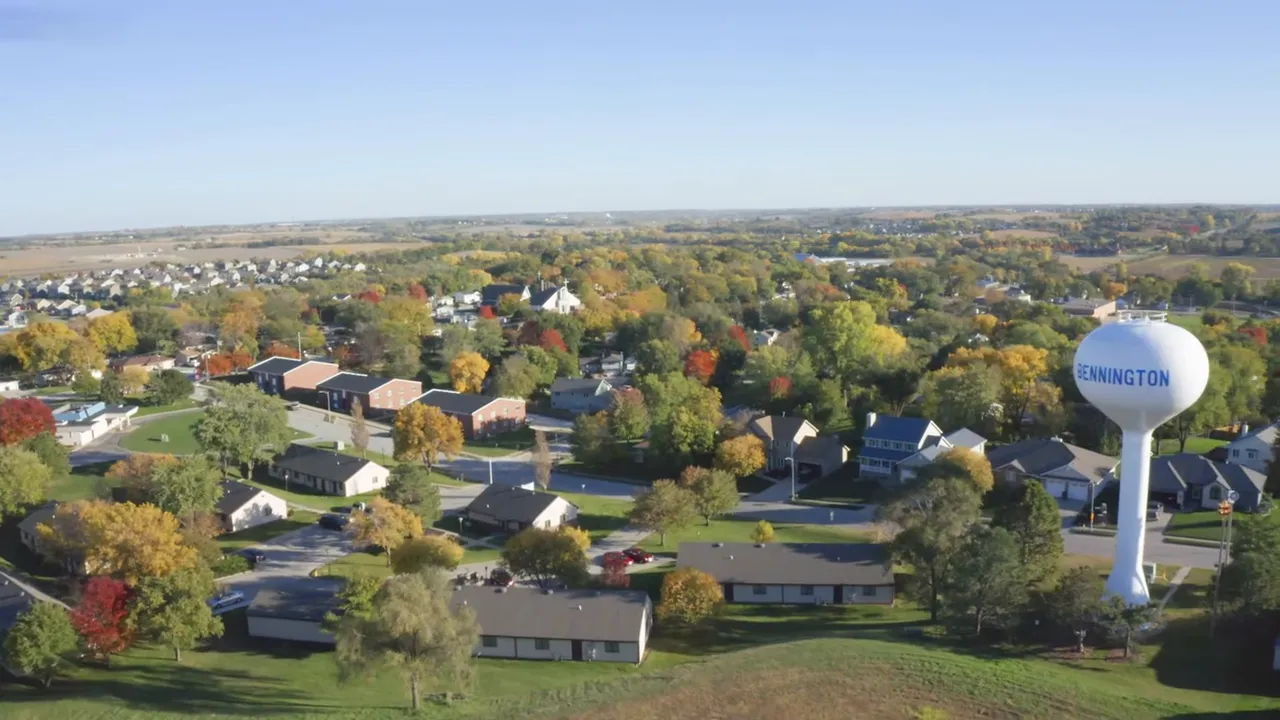 Wide drone view of Bennington neighborhood and water tower with fall-colored trees, homes and open fields.