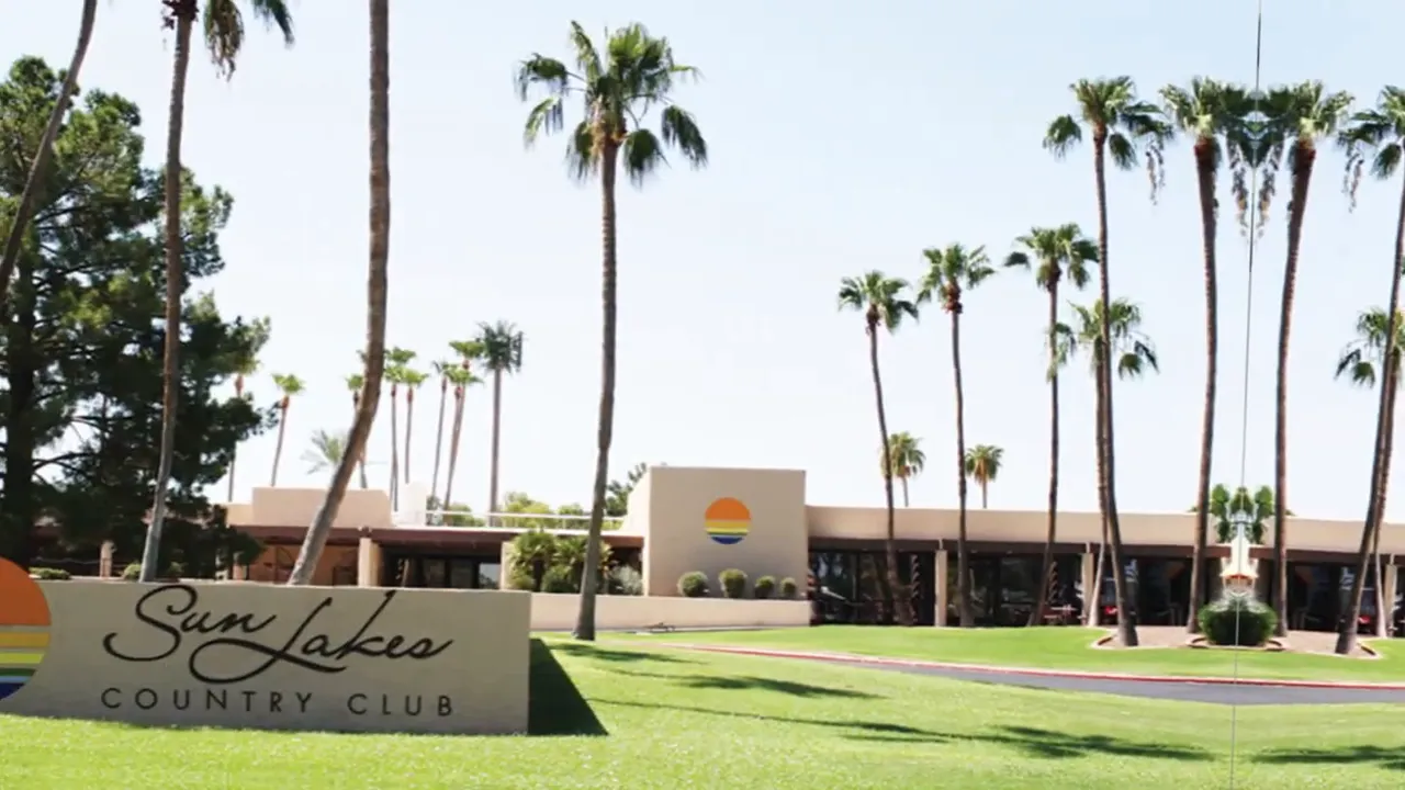 Sun Lakes Country Club entrance sign with palm trees and clubhouse in the background