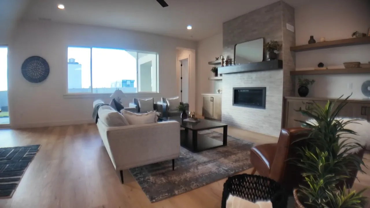 Main living area with sofa, armchairs, coffee table, fireplace with mantel, shelving and ceiling fan
