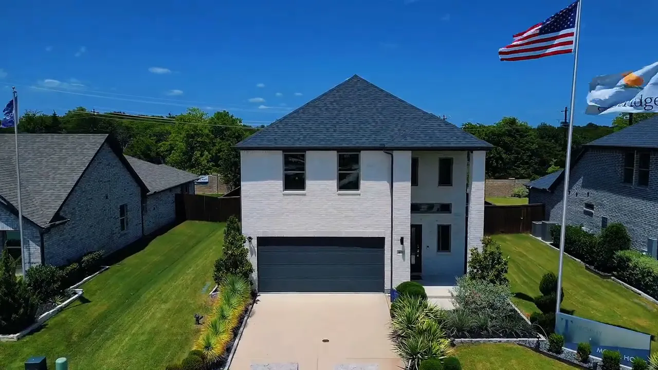 Front exterior of a two story white brick home with dark roof and driveway