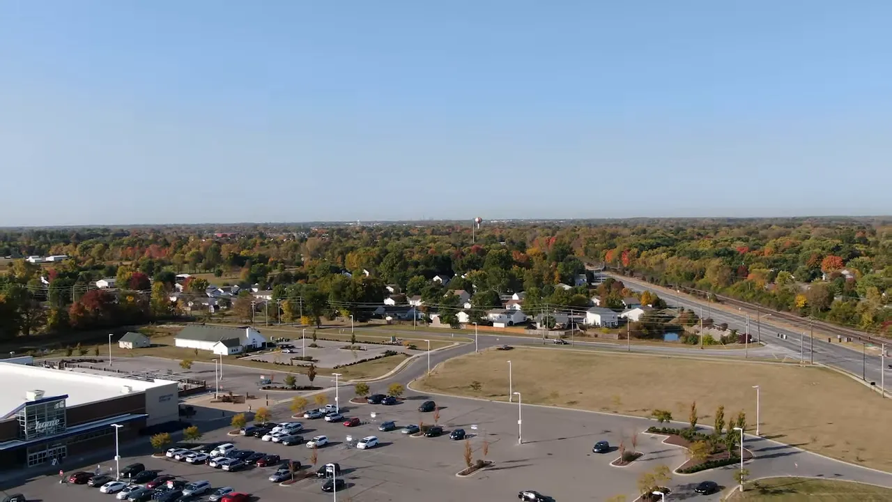 Aerial view of suburban development with parking lot, new homes, roads, and tree-lined horizon near Indianapolis.