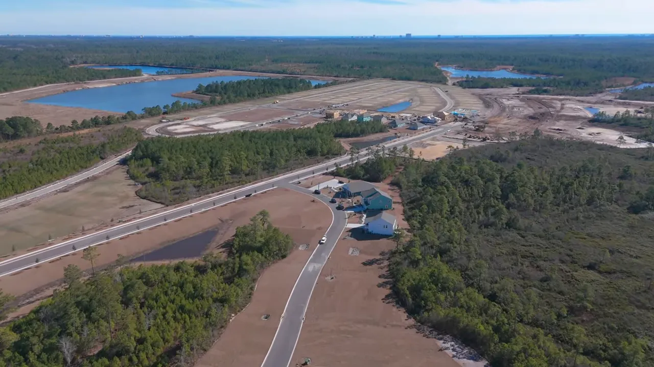 Drone aerial showing a large subdivision under construction with cleared home sites, infrastructure and ponds — clear view of the planned community.